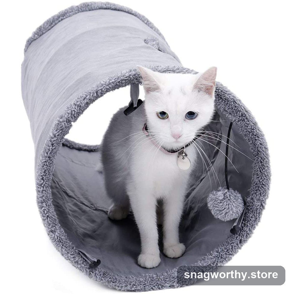 White cat sitting inside a grey collapsible crinkle tunnel with a pom-pom toy | Snagworthy.store