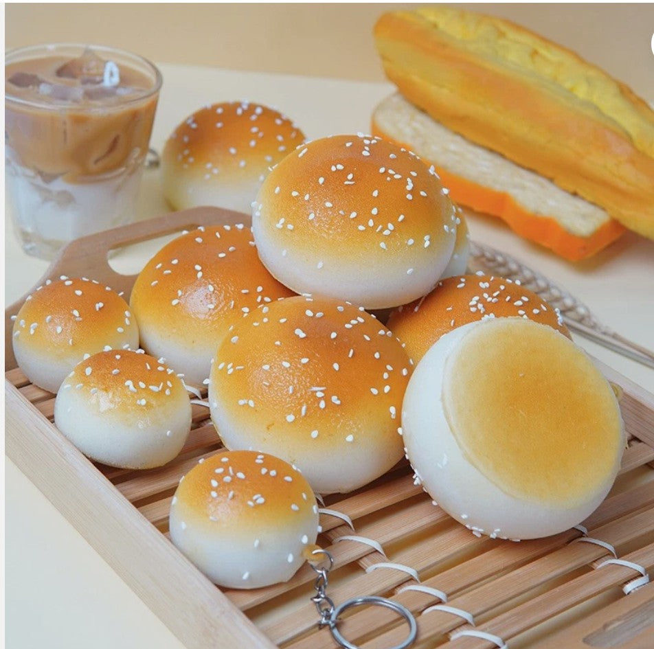 Realistic sesame bun squishy toys with keychain rings on a wooden tray